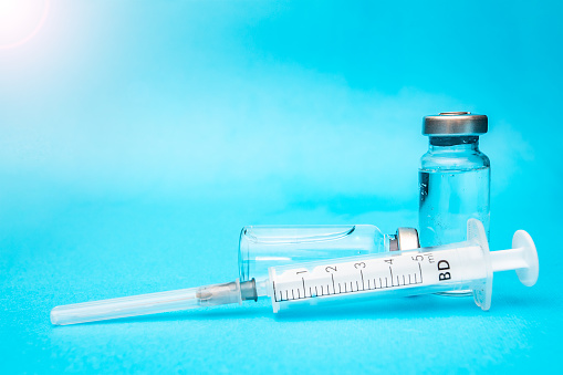 two ampoules of vaccine with a syringe on a blue background.