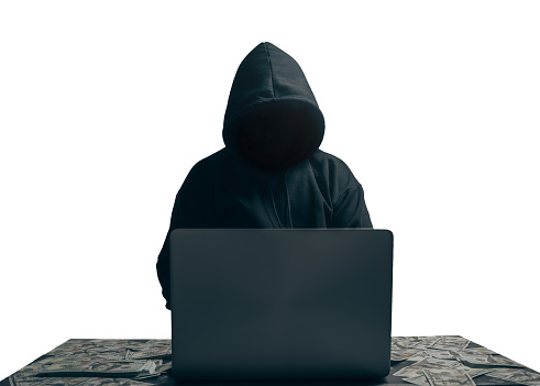 isolated of Unknown young man hacker sitting playing laptop with lots of money lying around.Concept Massive financial theft