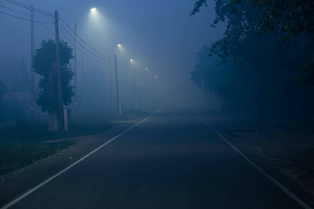 route dans la ville par une soirée sombre avec un brouillard épais, éclairé par des lampadaires led - fog road spooky mist photos et images de collection