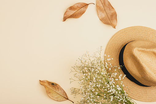 Female straw hat, autumn leaves and gypsophila bouquet on neutral beige background. Top view, flat lay, copy space.