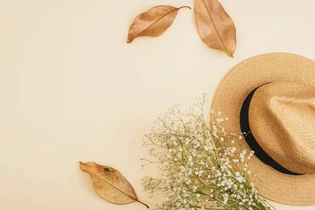 Female straw hat, autumn leaves and gypsophila bouquet on neutral beige background. Top view, flat lay, copy space.