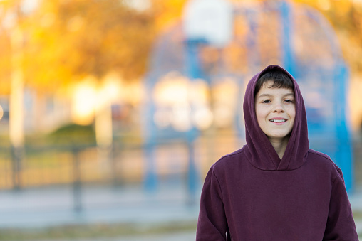 Outdoor handsome boy portrait. Teen boy in hood over park nature background.