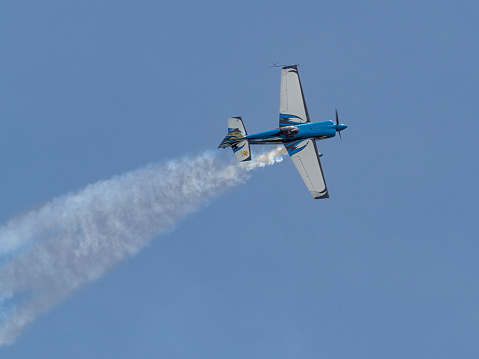 Hillsboro, Oregon, USA - May 22, 2022 :  Melissa Burns in her Edge 540 aerobatic airplane is flying with a white trail of smoke. The Air Show in Hillsboro, Oregon is a very popular event each year. The theme for 2022 was “She Flies with her own wings.” All performers, pilots and announcers were women. Hillsboro is a suburb of the city of Portland, Oregon.
