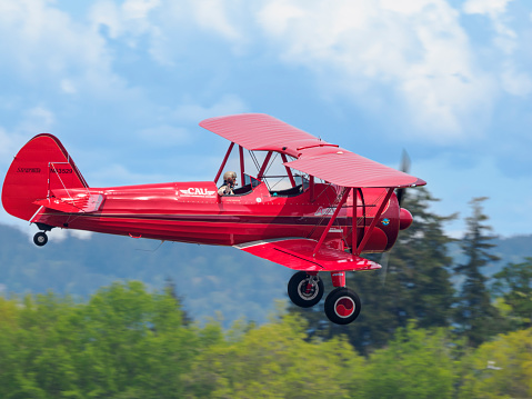 Hillsboro, Oregon, USA - May 22, 2022 :  Vicky Benzing, PhD and 1940 Boeing Stearman aerobatic airplane waving at the airshow crowd. The Air Show in Hillsboro, Oregon is a very popular event each year. The theme for 2022 was “She Flies with her own wings.” All performers, pilots and announcers were women. Hillsboro is a suburb of the city of Portland, Oregon.