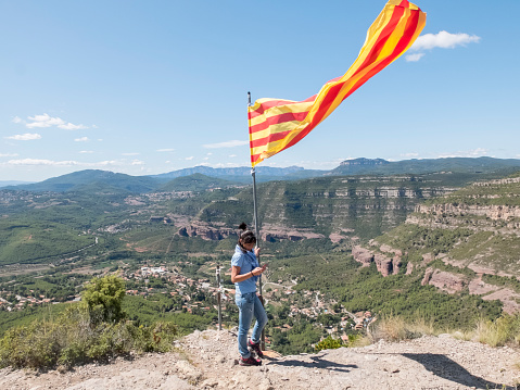 A woman holding a Catalonia flag on top mountain while using mobile