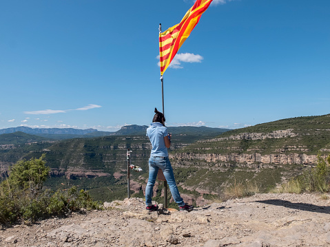 A woman holding a Catalonia flag on top mountain while using mobile
