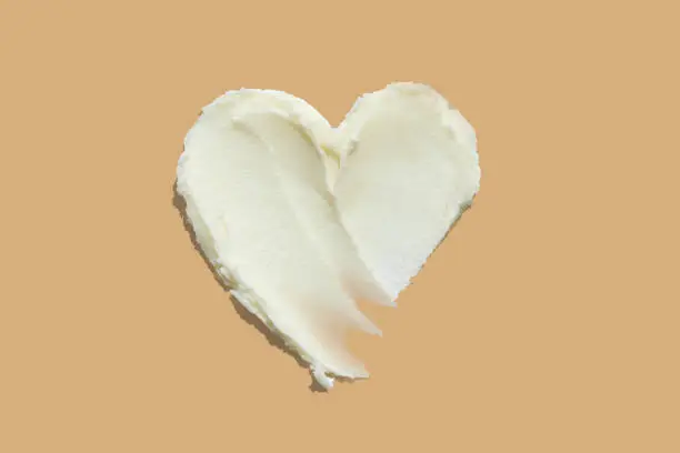 Photo of Heart shape from thick shea butter cream moisturiser on brown beige background. Skin care product texture heart