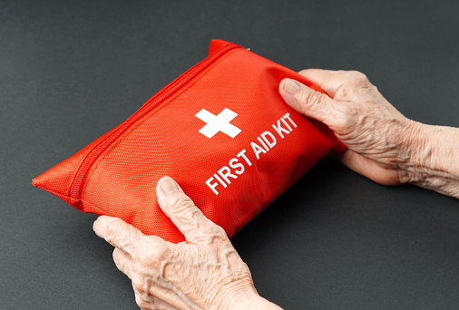 Old wrinkled hands holding first aid kit.