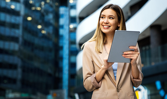 Portrait of a successful young business woman using digital tablet in front of modern business building