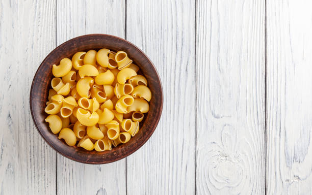 pasta rigata a tubo crudo in ciotola di ceramica su fondo di legno bianco - italian cuisine dry pasta directly above foto e immagini stock