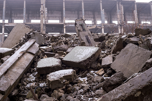 A pile of large concrete fragments against the background of the destroyed frame of the building in a hazy haze. Background.