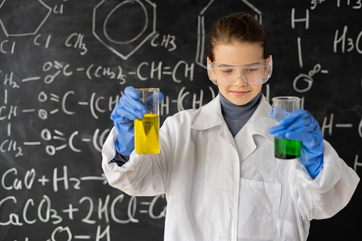 young girl making science experiments in laboratory. student doing a chemical experiment while making analyzing and mixing liquid in glass flasks at science class. education concept