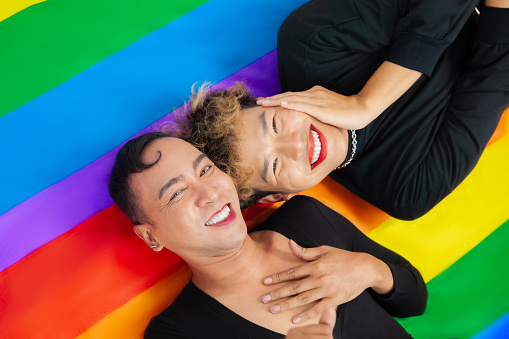 Photo of Happy asian gay couple lay down on pride flag rainbow background. lgbtq and lgbtq+ concepts