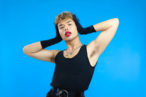 Portrait of asian gay man posing over isolated blue background. Transgender Gay Pride LGBTQ+ concepts