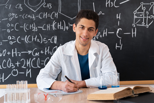 muslim young teacher leading chemistry lesson at school, chemistry science and experience in college lab, arabic student sitting at table looking at camera