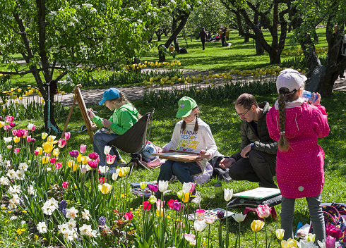 Moscow, Russia - May 22, 2022:  Young artists in the open air - children draw blooming tulips in Kolomenskoye Park. Sunny day in May.