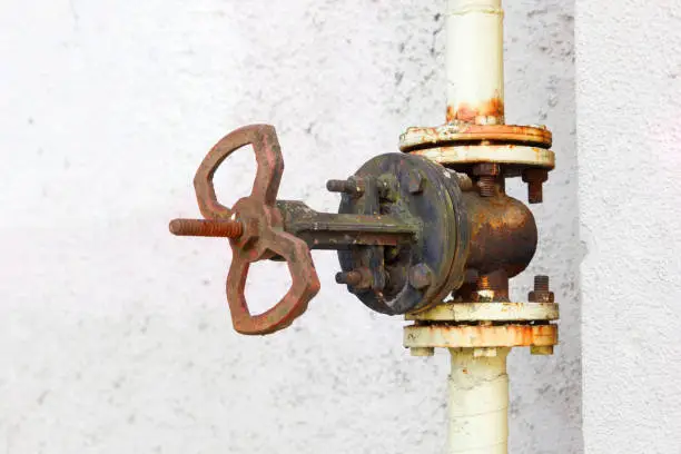 Photo of Rusty pipe valve on white wall background.