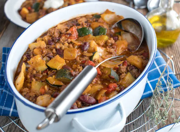 Fresh and homemade cooked healthy and delicious family dish with minced meat, white cabbage, vegetables and kidney beans. Served in a rustic and white stew pot with ladle on kitchen table background
