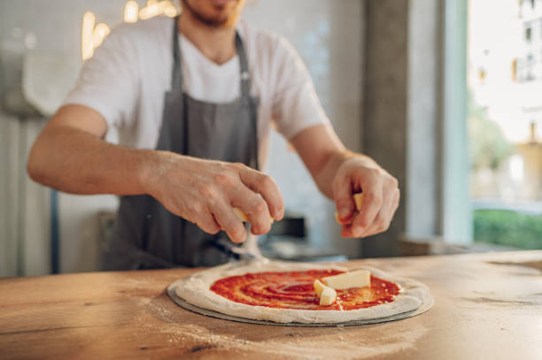 istock Man worker in a pizza place placing ingredients on pizza dough 1402083434