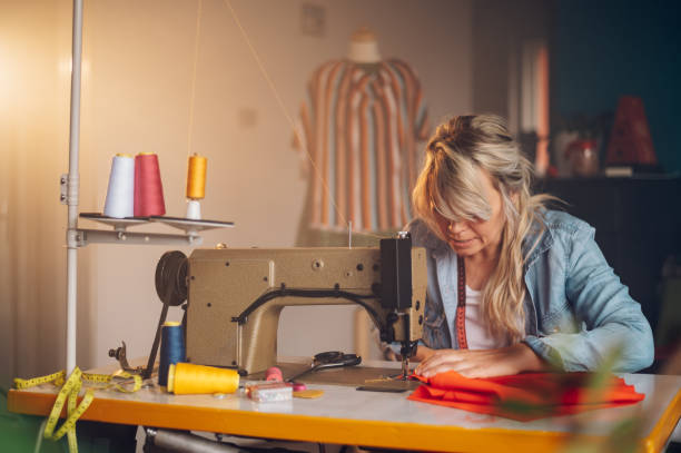 istock Tailor woman sitting and sewing on a sewing machine a in studio 1402083443
