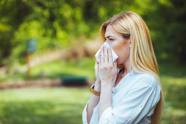 Spring allergy concept Young pretty woman blowing nose in front of blooming tree. Spring allergy concept. Attractive young adult woman coughing and sneezing outdoors. Sick people allergy or virus influenca concept. nose flower stock pictures, royalty-free photos & images