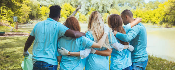 Group of volunteers embracing in park Volunteering, people and ecology concept. Group of volunteers embracing in park, back view, copy space non profit organization stock pictures, royalty-free photos & images