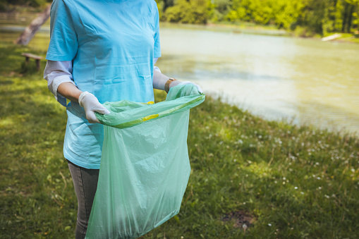 Young female unrecognizable volunteer with trash bags in the forest, helping to clean forest from litter. A woman is part of the unprofitable organization for cleaning and recycling garbadge.