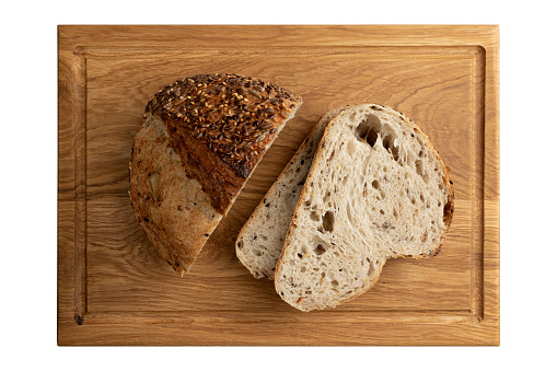 top view of fresh sliced homemade bread with golden crispy crust on wooden board isolated on white background, organic loaf with sunflower and linen seeds close-up