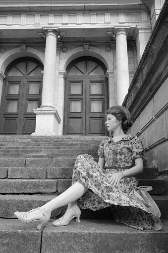 Fashion style portrait. Young elegant woman in long dress posing at stairway against old city building monochrome