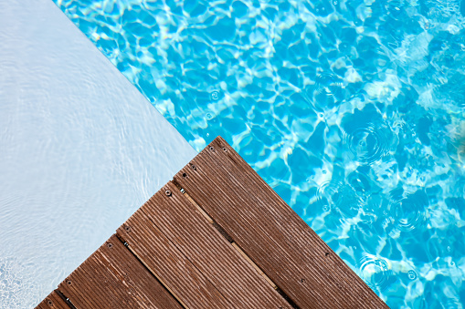 Wooden platform on swimming pool background. Pool background wallpaper. Space for text.