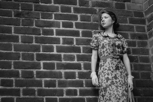 Fashion style portrait. Young elegant woman in red long dress posing at old city building monochrome