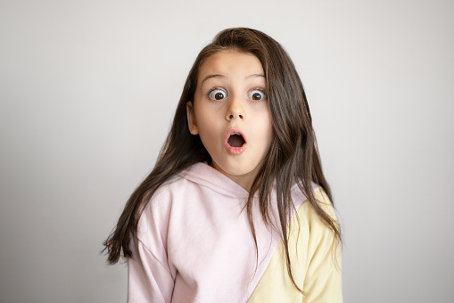 Cute little girl making a shocked face over gray background