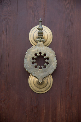 Old decorative round brass door knocker on wood door closeup\