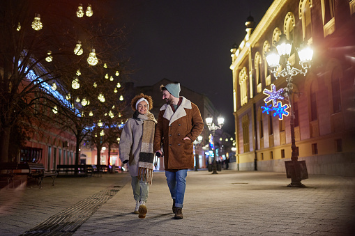 Young happy couple walking during Christmas night on the city street.