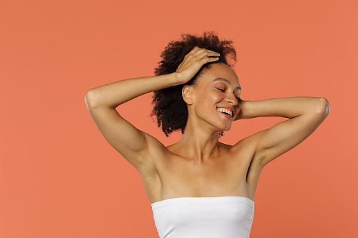 Portrait of a beautiful African American woman with curly hair in her 30s and  wearing no make up trying a new skincare routine with orange background in white shirt stock photo