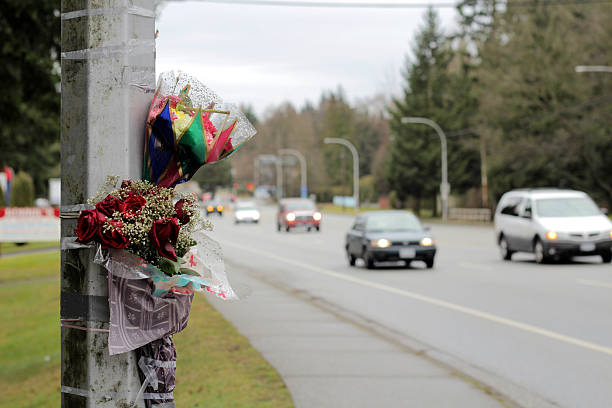 Cars Pass By Roadside Memorial Accident Scene Flowers are taped against a light standard by the side of a busy street following a fatal auto accident serving as a reminder for all of us to "slow down" and drive safe! See ROADSIDE MEMORIAL clips here! truck in rain stock pictures, royalty-free photos & images