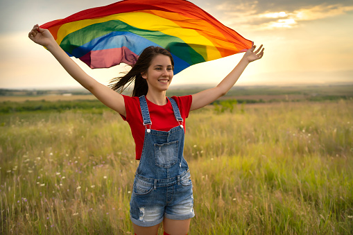 LGBT girl holding a rainbow flag against the wind and smiling