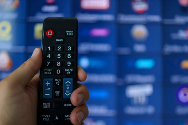 istock Smart tv and hand pressing remote control.Hand holding TV remote control with a television in the background. Close up. 1402104380