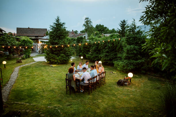여름에 야외에서 식사하는 사람들의 광각 사진. 멋진 정원에서 식사를하는 친구와 가족의 큰 그룹 - 가든파티 뉴스 사진 이미지