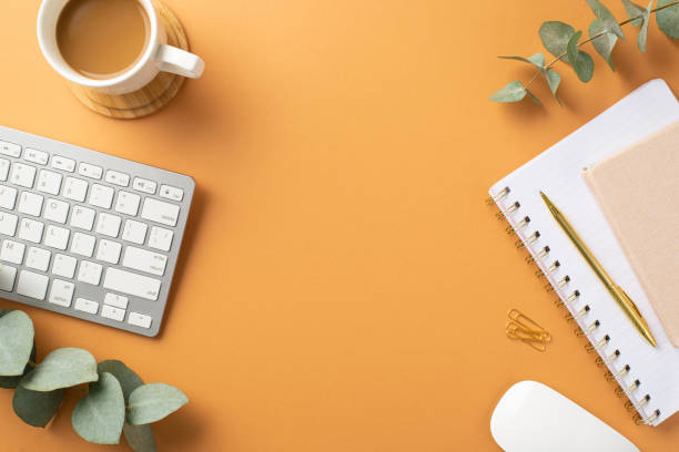 istock Business concept. Top view photo of workspace white keyboard planners computer mouse stationery gold pen clips cup of coffee on wooden stand and eucalyptus on isolated orange background with copyspace 1402105724