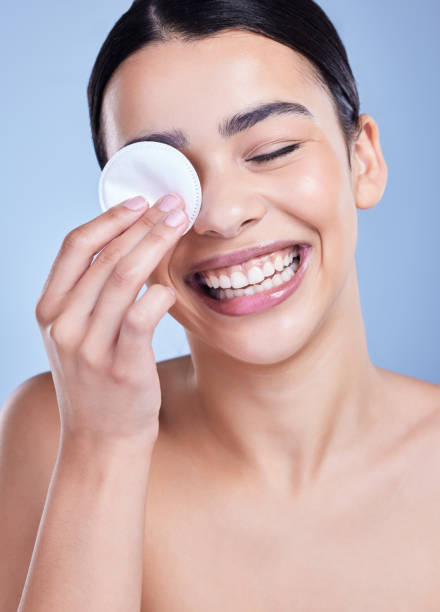 istock A beautiful smiling mixed race woman using a cotton pad to remove makeup during a selfcare grooming routine. Hispanic woman applying cleanser to her face against blue copyspace background 1402105789