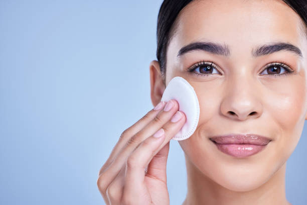 istock Studio Portrait of a beautiful mixed race woman using a cotton pad to remove makeup during a selfcare grooming routine. Hispanic woman applying cleanser to her face against blue copyspace background 1402105983