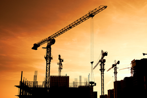 Silhouette of tower cranes and high-rise buildings under construction at construction site at yellow sunset