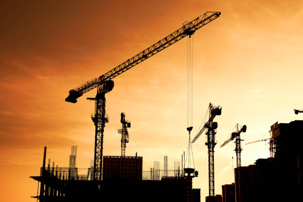 Silhouette of tower cranes and high-rise buildings under construction at construction site at yellow sunset Silhouette of tower cranes and high-rise buildings under construction at construction site at yellow sunset. Orange yellow sky. Shooting the building new houses in the city crane stock pictures, royalty-free photos & images