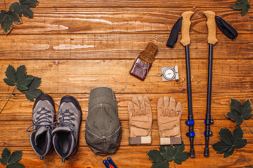 Hiking gear concept on wooden background decorated with leaves and clothing