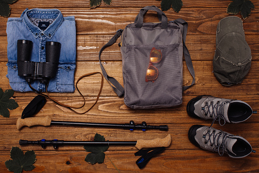 Backpack, shirt, boots, binoculars, thermos and hat on wooden background captured from above
