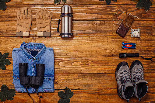 Backpack, shirt, boots, binoculars, thermos and hat on wooden background captured from above