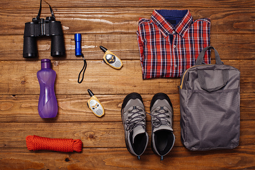Shirt, binoculars, thermos, hat, water bottle, sunglasses and multifunctional knife on wooden background captured from above