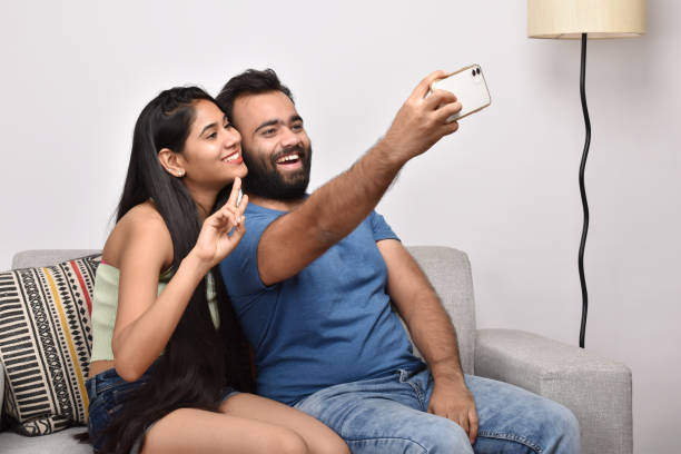 istock Young couple sitting on sofa and taking selfie 1402110017