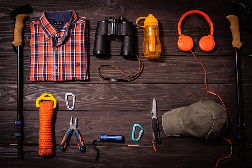 Shirt, boots, binoculars, thermos, hat protective gloves, robe, bandana, hiking pole and sunglasses on wooden background captured from above copy space